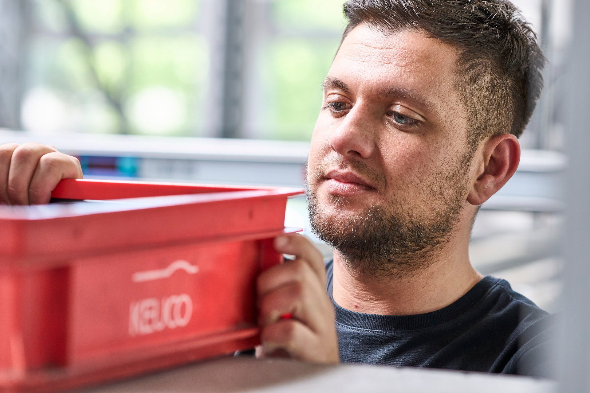 Mitarbeiter fokussiert eine rote Box mit KEUCO Logo in seinen Händen